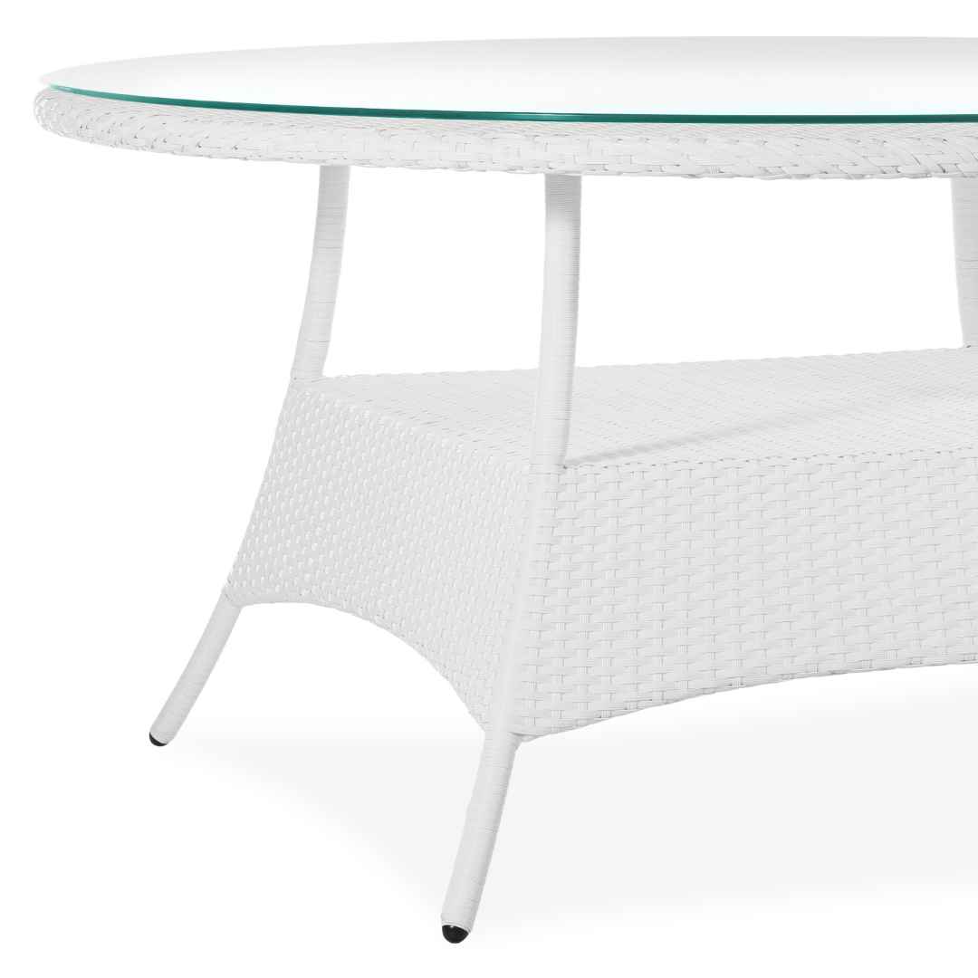 Detail bílého ratanového stolu BALINA Terico: okraj oválné skleněné desky, výplet z umělého ratanu a tvarovaná noha.